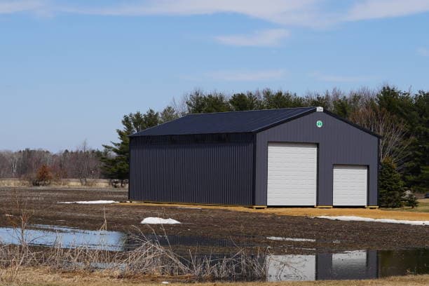 Black metal workshop building beside a pond